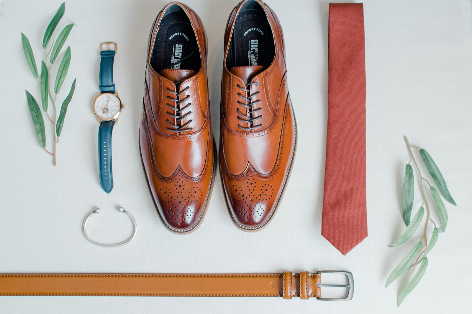 Shoes, a watch, a tie, and a wrist band against a slate white background